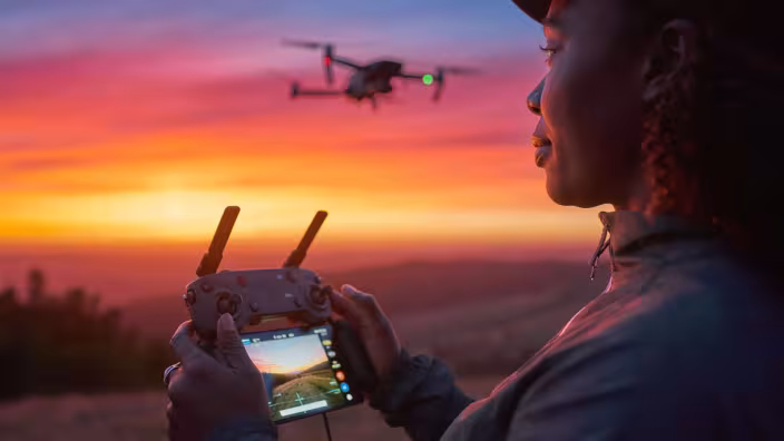 Dramatic wide-angle shot of a professional drone pilot operating a high-end camera quadcopter in open golden hour light